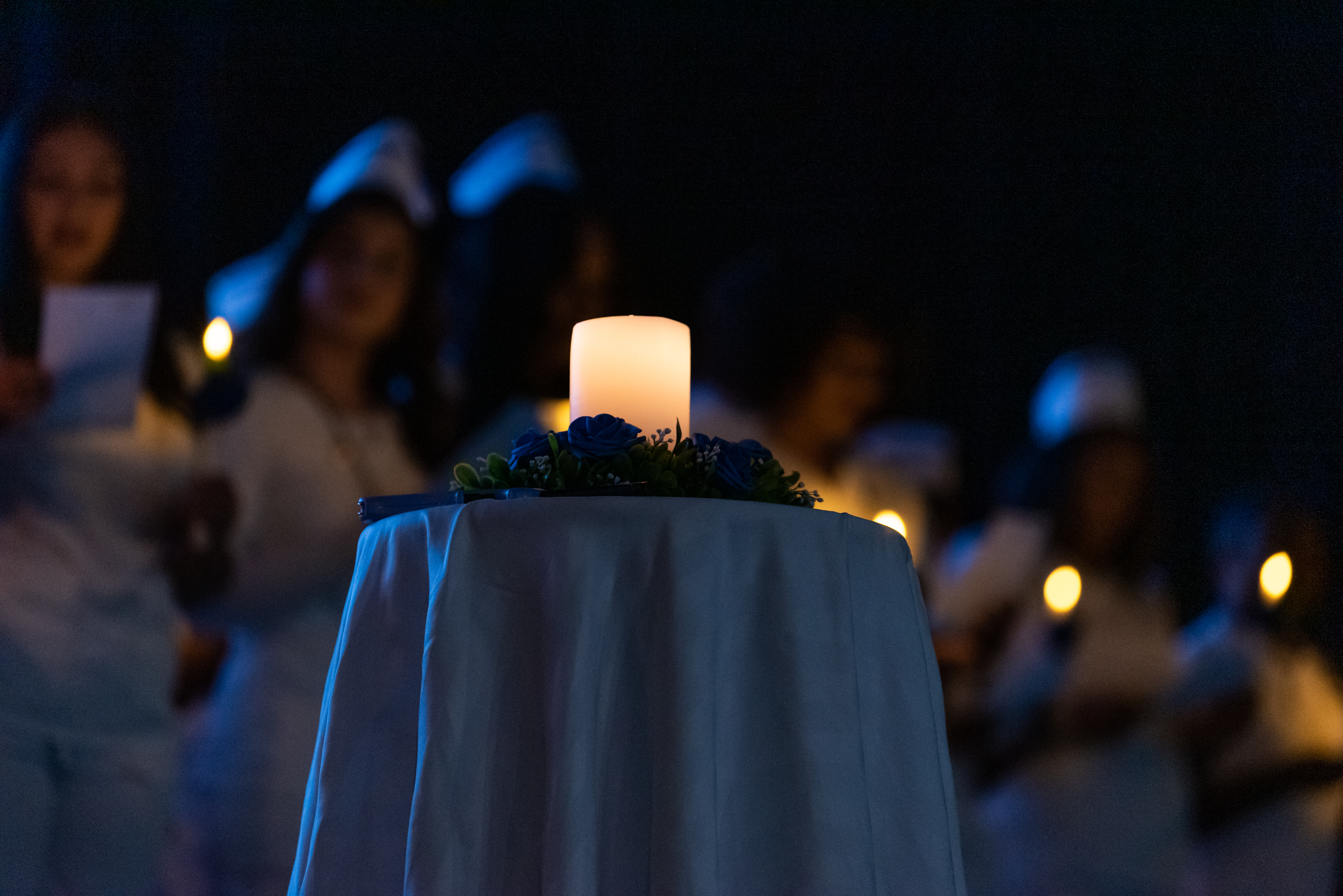 Lit candle on a table with blurred images of nursing students in background
